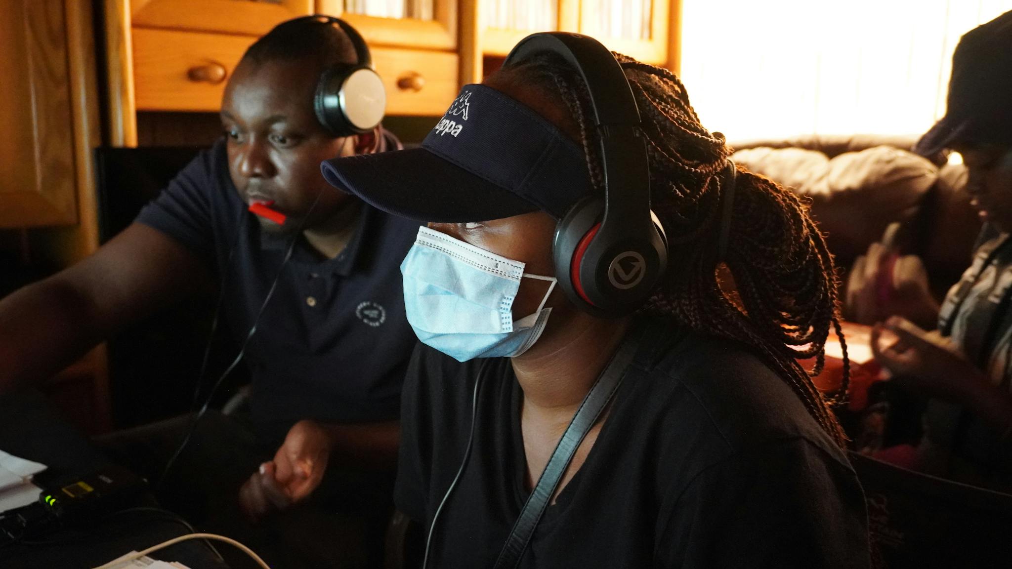 People in a shared workspace wearing headphones and masks, focusing on a project.